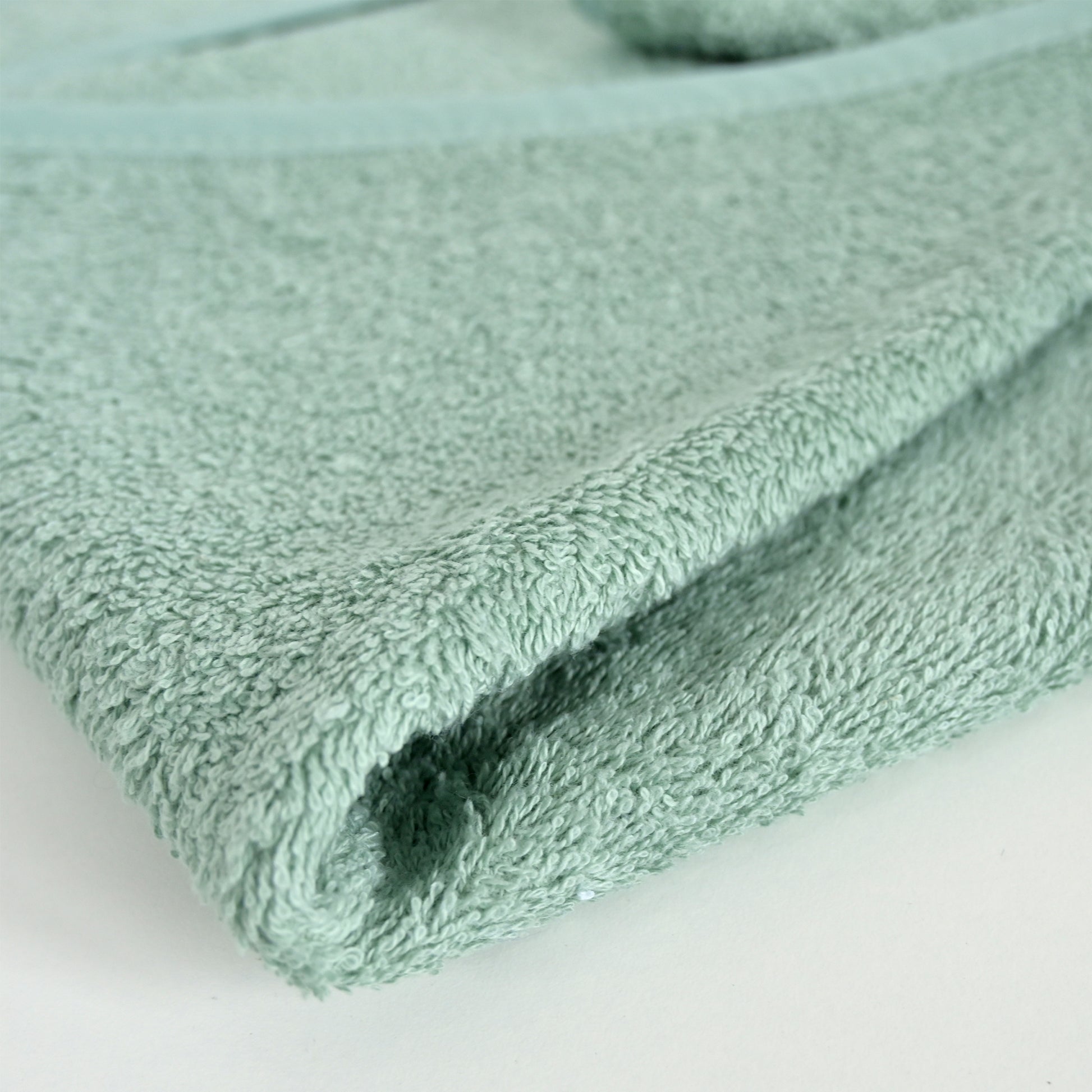 A close-up of a folded mint green terry cloth towel showing its soft, textured surface on a plain white background.