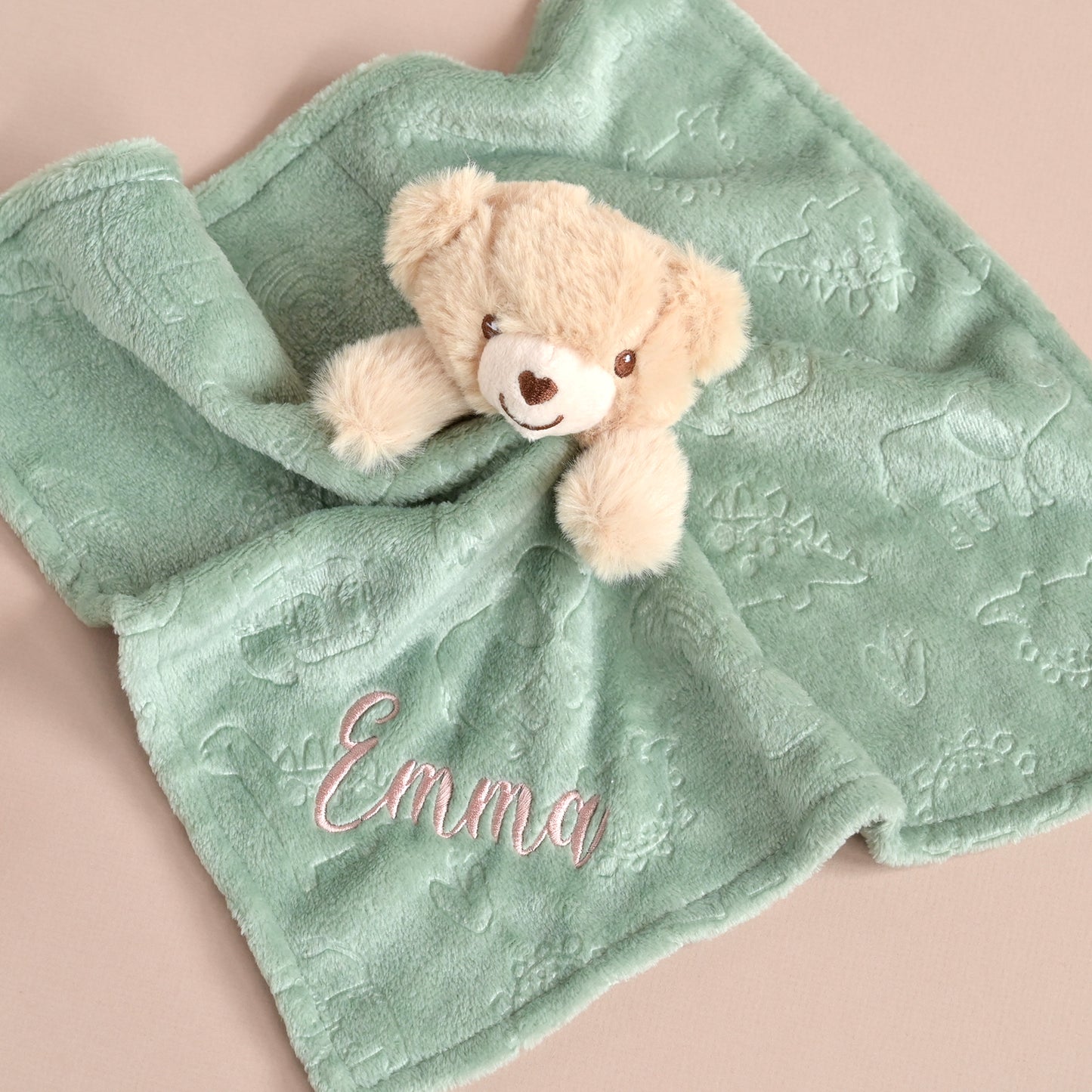 A personalized baby lovey blanket in mint green, featuring an embroidered teddy bear plush and the name 'Emma' stitched in pink on the front, set against a solid pale pink background.
