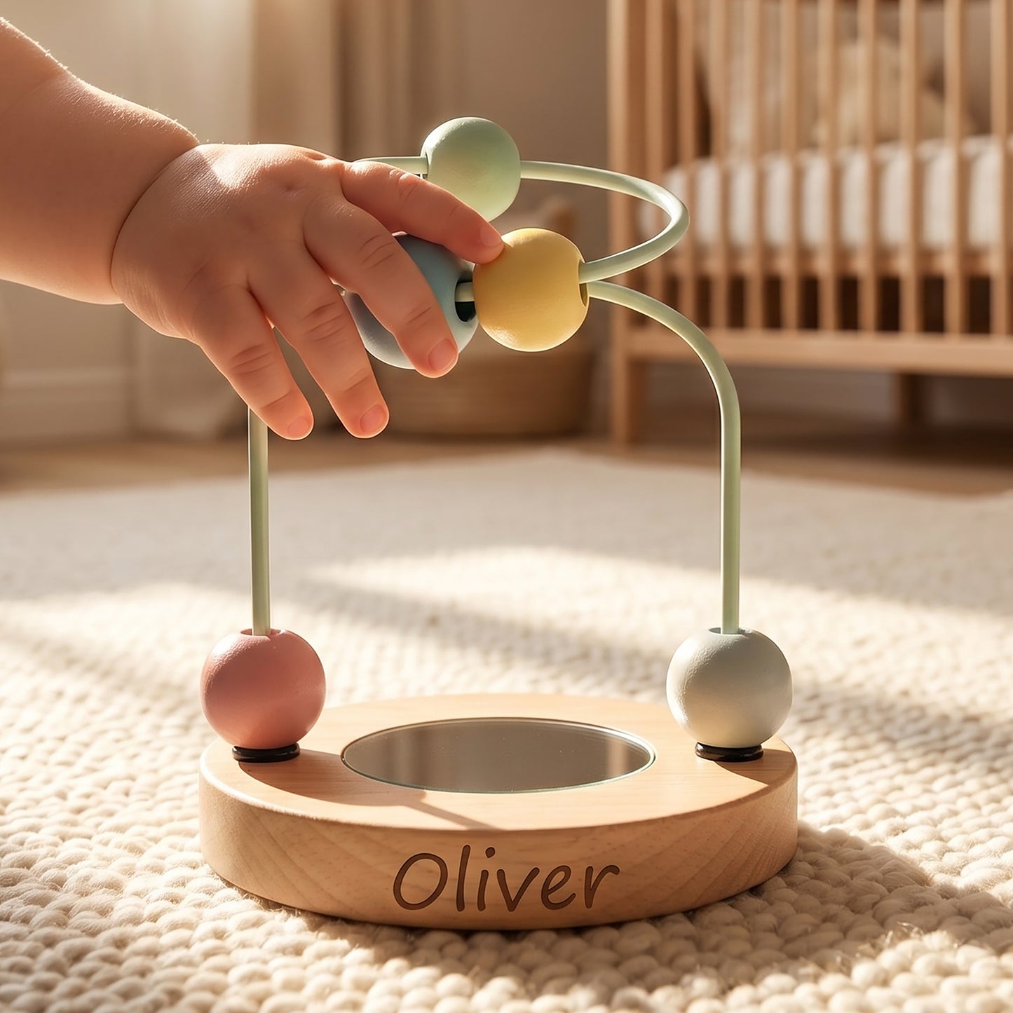A baby's hand plays with a personalized wooden bead maze toy engraved with the name 'Oliver'. The toy features a light natural wood base, pastel-colored wooden beads in green, yellow, pink, and white, and a small metal cup in the center.