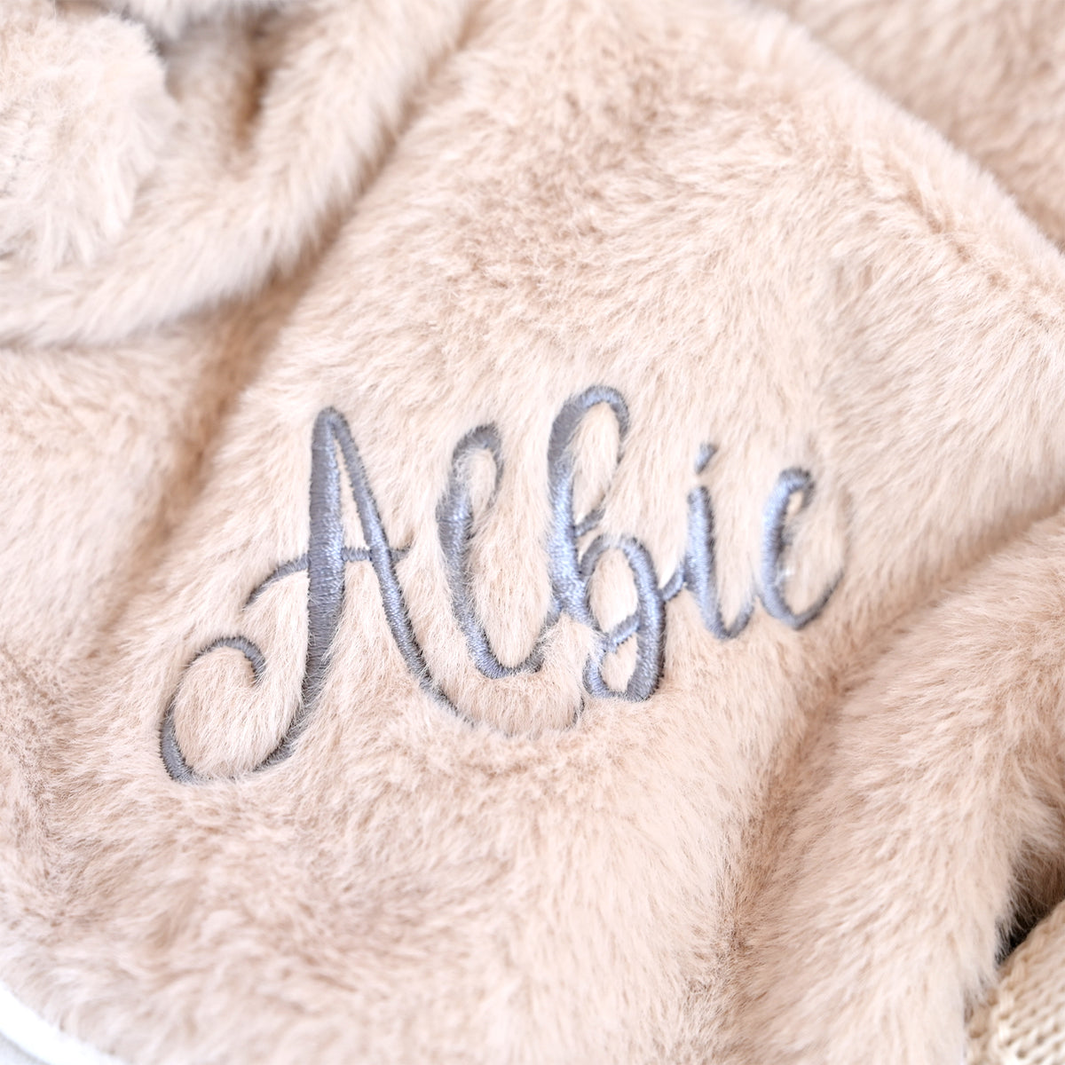 Close-up of a soft beige faux fur blanket with the name 'Albie' embroidered in gray cursive script.