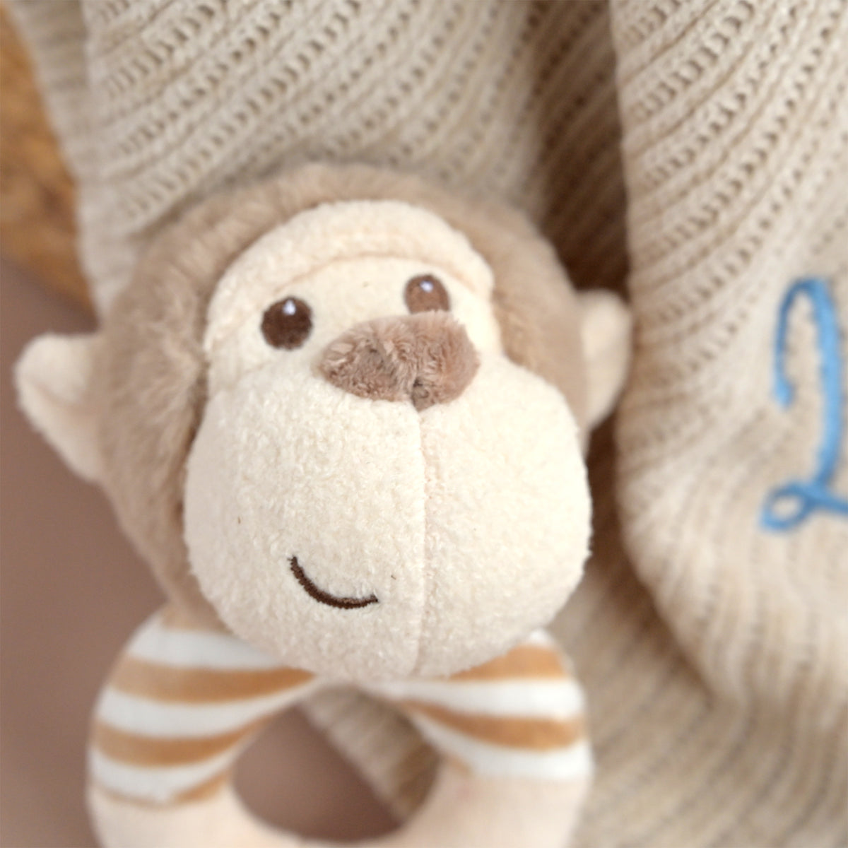 Close-up of a plush monkey toy attached to a knitted beige baby blanket with a blue embroidered number 2.