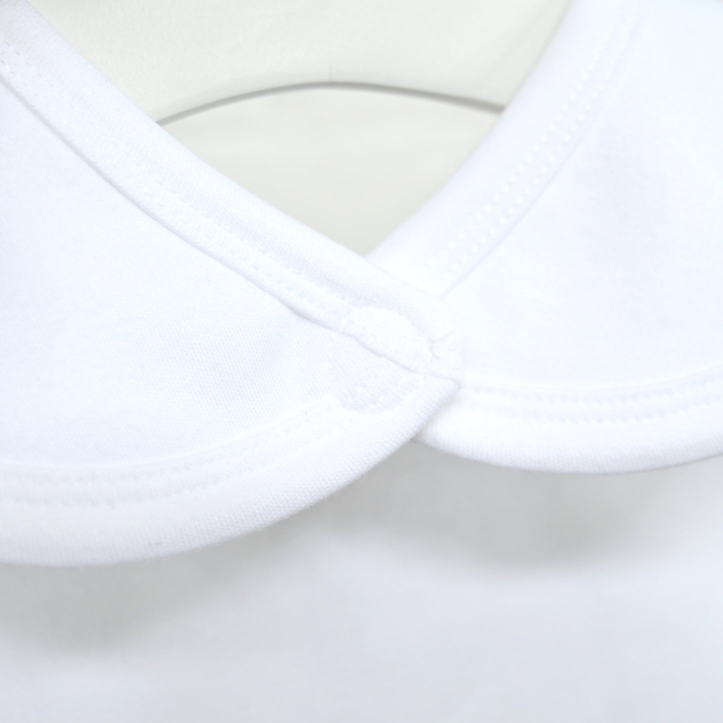 Close-up of a white baby garment with a wide, rounded Peter Pan collar and fine stitching.