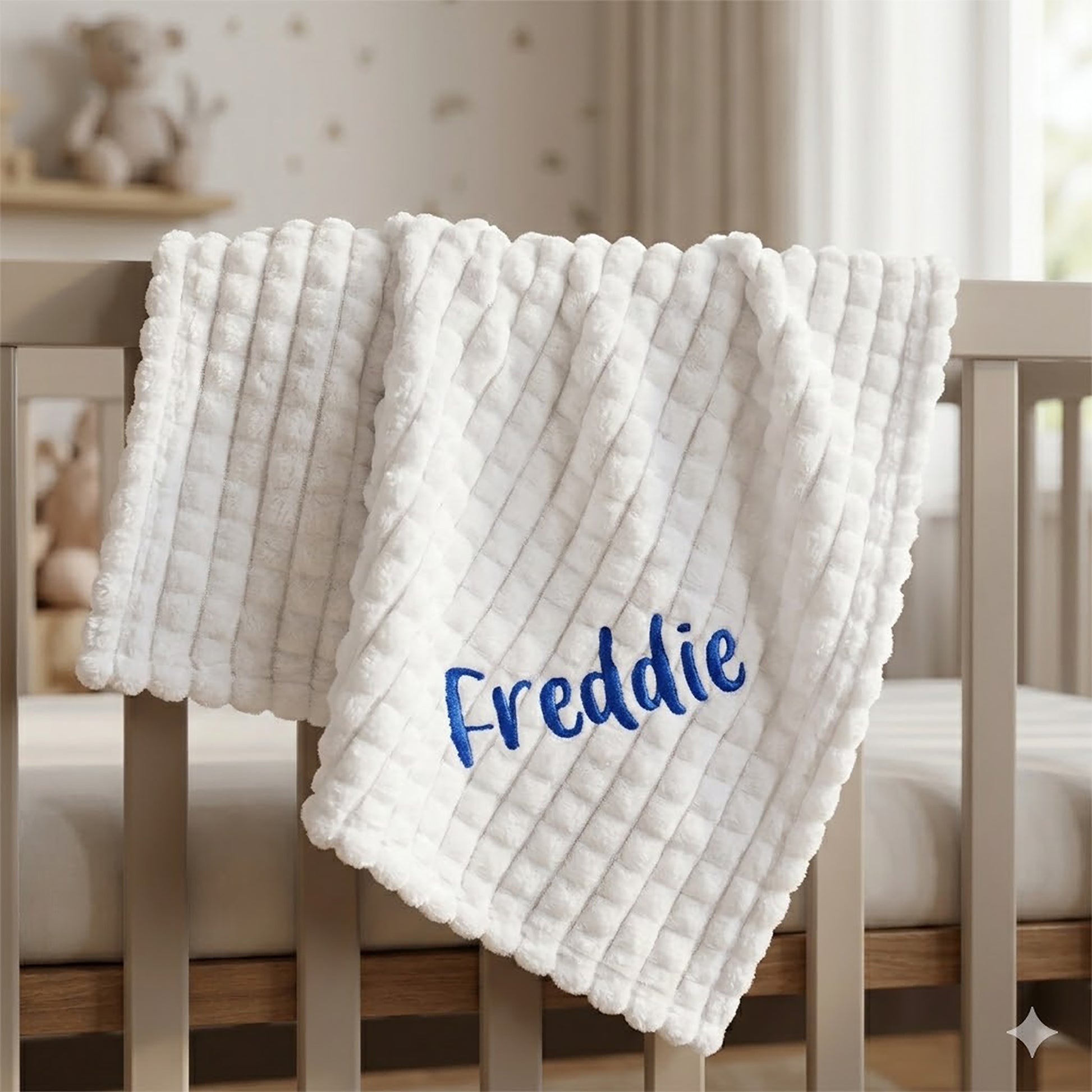 White ribbed fleece baby blanket hanging over a wooden crib rail, personalised with the name Freddie in navy embroidery.