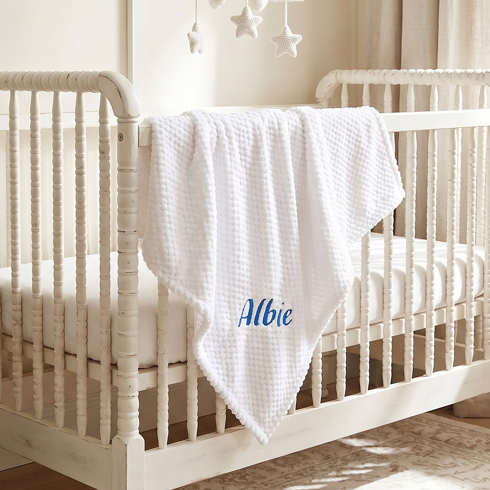 Grey waffle-knit baby blanket personalised with the name William embroidered in blue, hanging over a wooden cot rail.