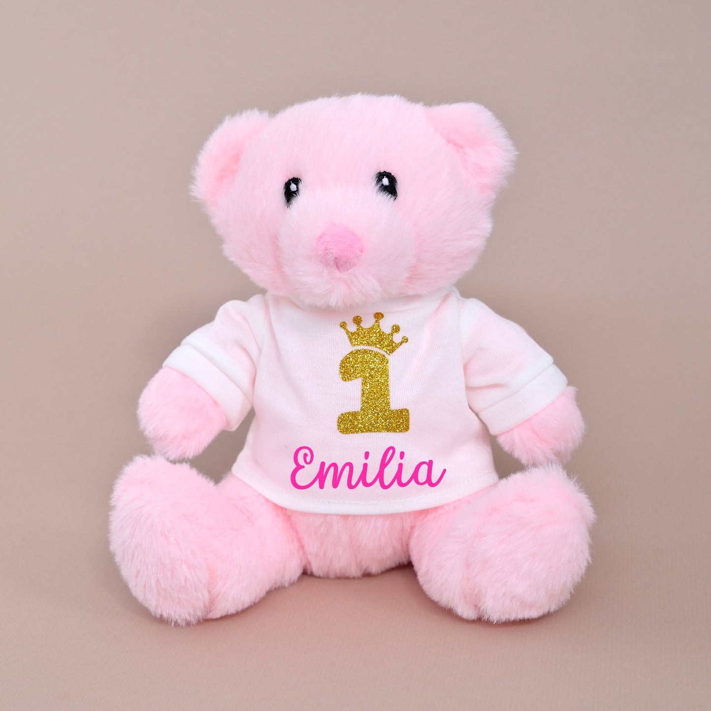 Pink teddy bear soft toy wearing a white t-shirt printed with a gold glitter "1" and crown, personalised with the name Emilia, 