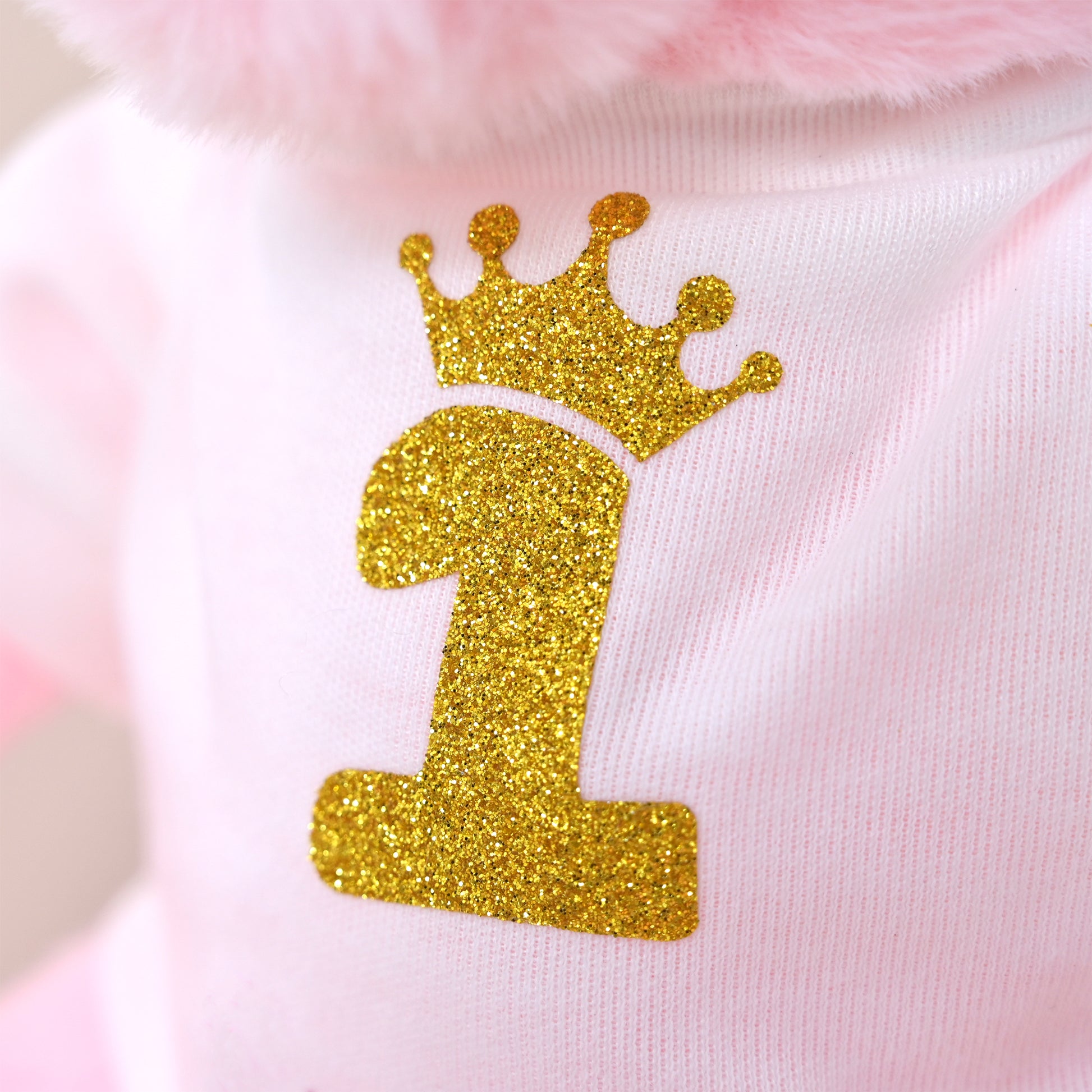 Close-up of a light pink garment with a glittery gold number 1 and crown applique on the front.