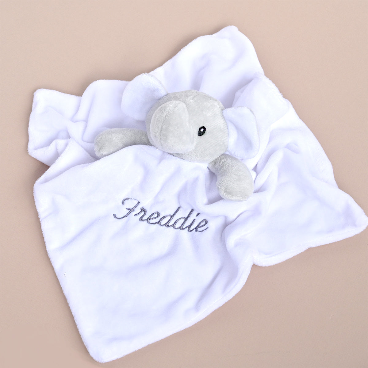 A white plush baby lovey blanket with an embroidered gray elephant and the name 'Freddie' in gray script, shown on a solid beige background.