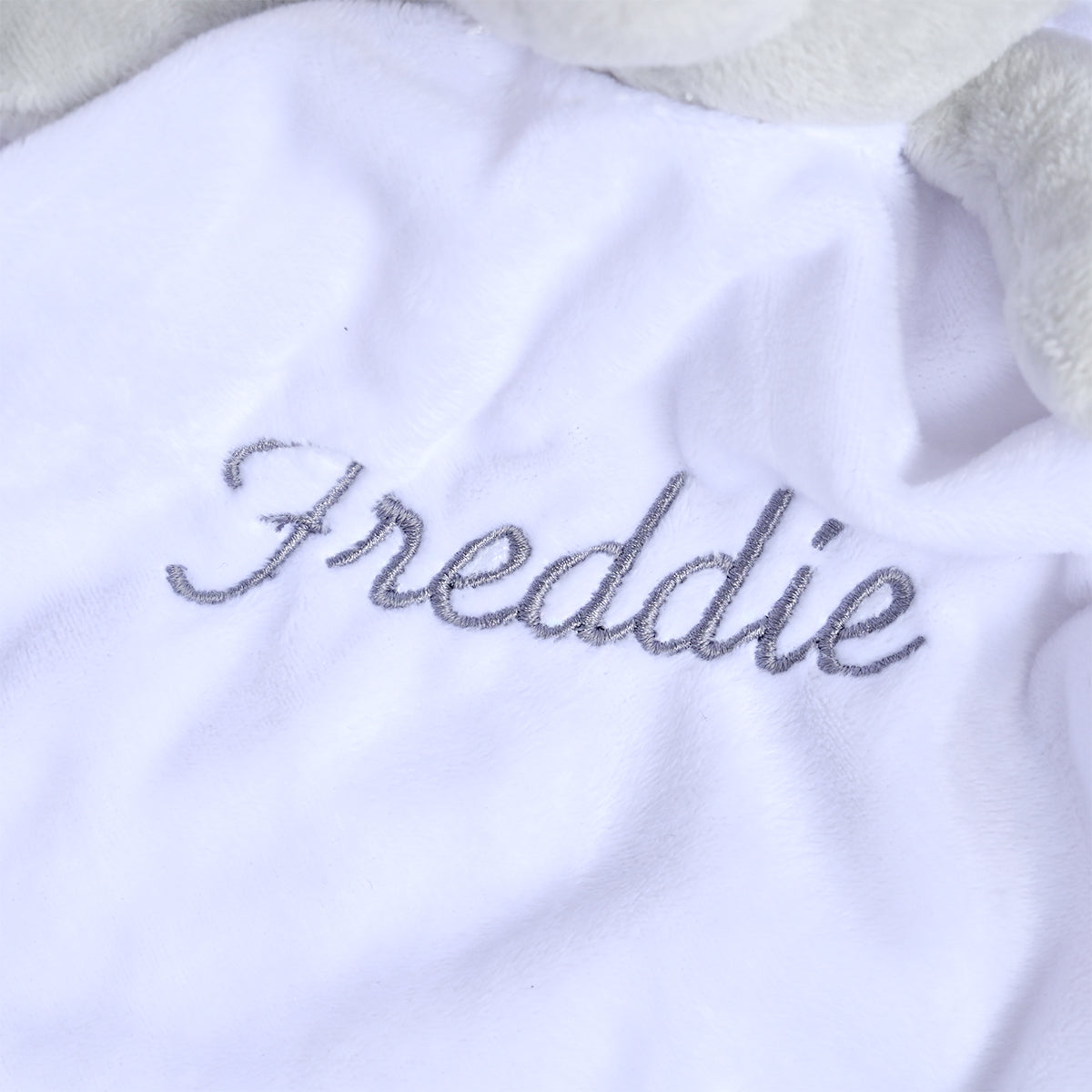 Close-up of a white plush blanket or pet bed with the name 'Freddie' embroidered in gray script across the front.