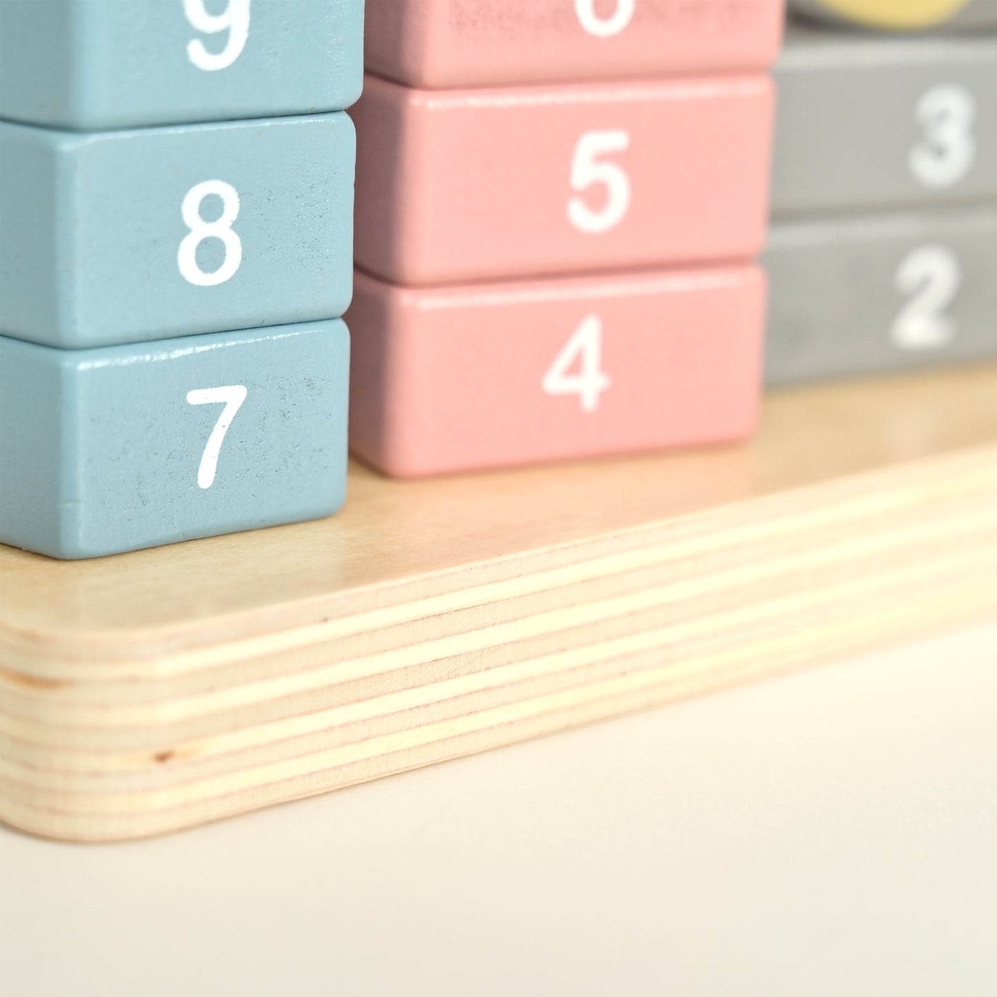 Close-up of wooden number blocks stacked on a light wood base, with pastel blue, pink, and gray pieces showing numbers 7, 8, 9, 4, 5, and 3.