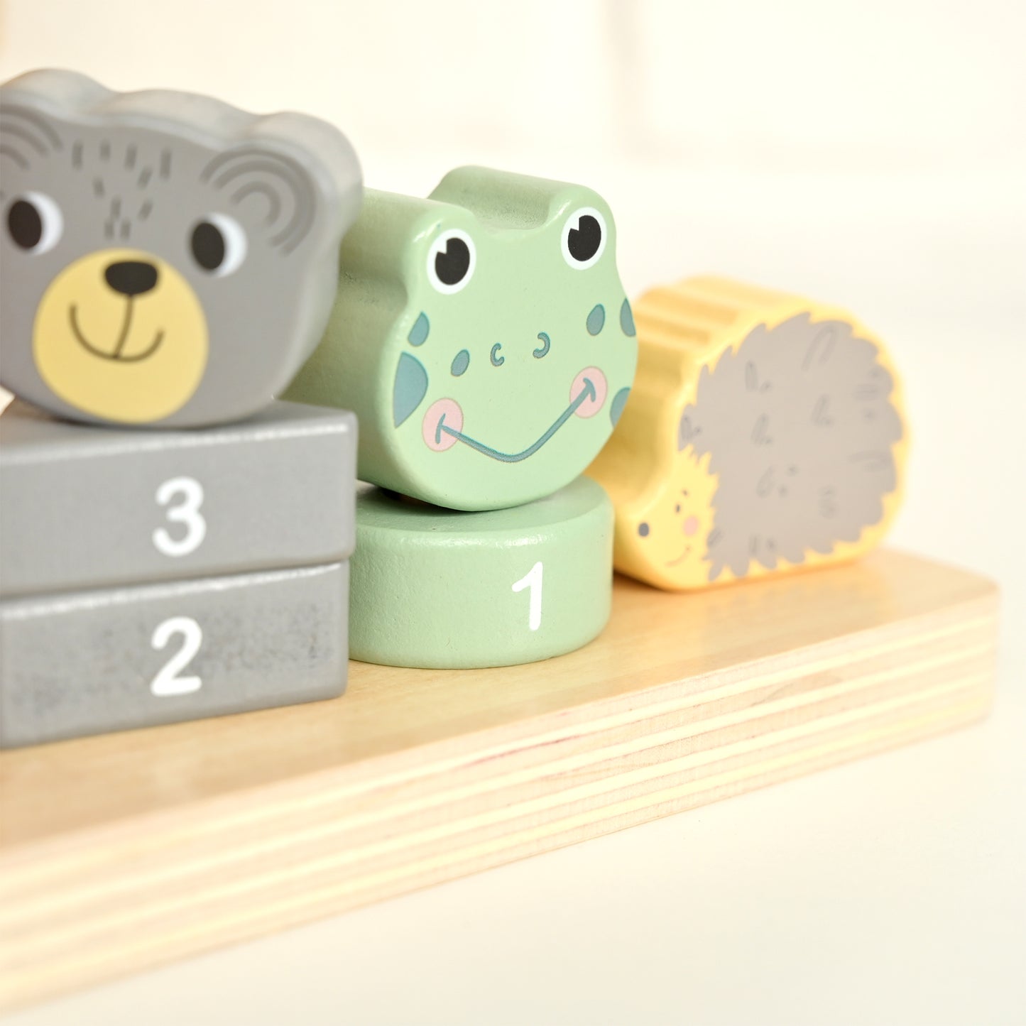 A close-up of a wooden Montessori number and shape sorter toy with animal-shaped blocks, including a gray bear, a green frog, and a yellow cylinder, arranged on a light wood base.