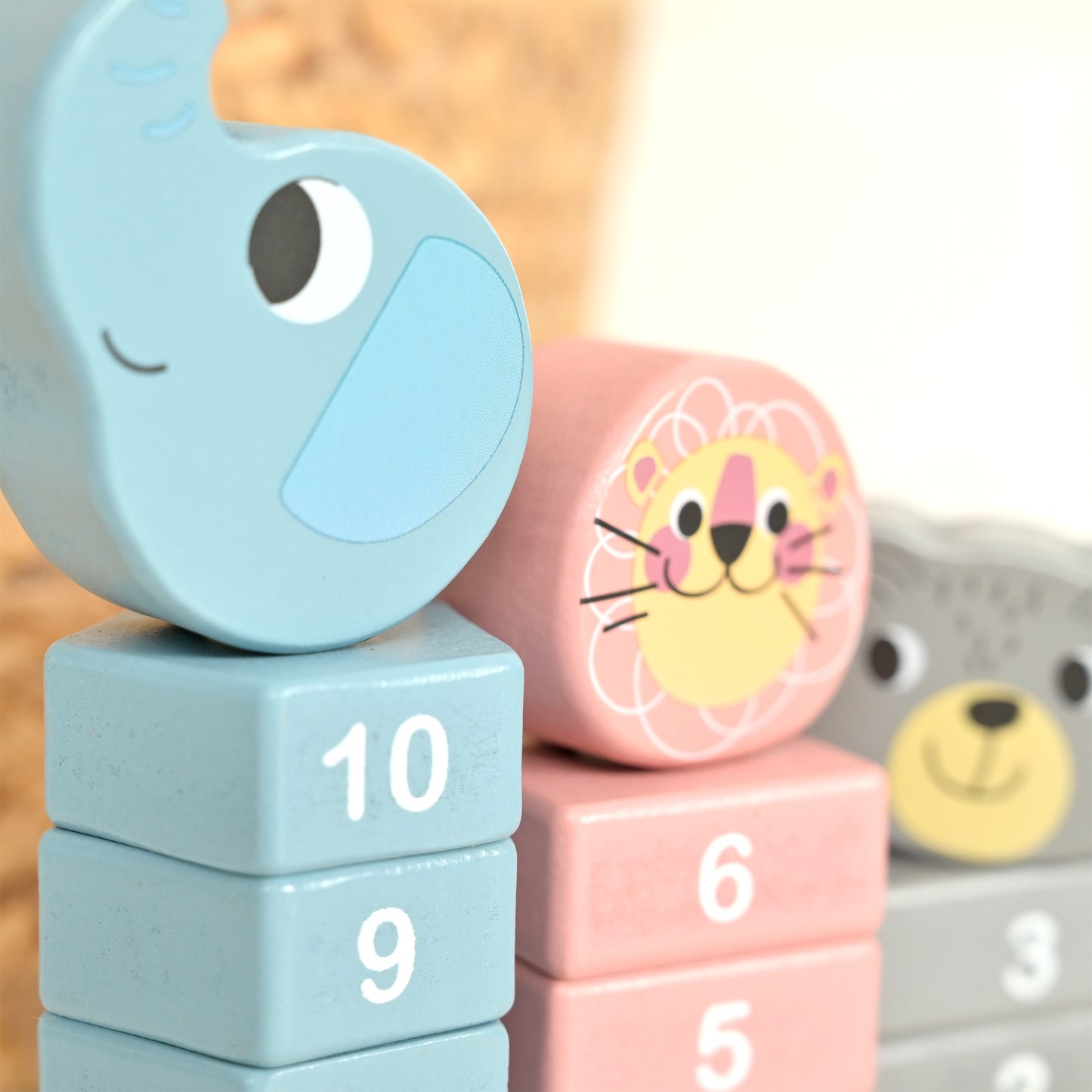 Close-up of colorful wooden animal and number blocks stacked together, including a light blue elephant head on top of a stack with the numbers 10 and 9, a pink lion face on a stack with the number 6, and part of a gray bear block in the background.